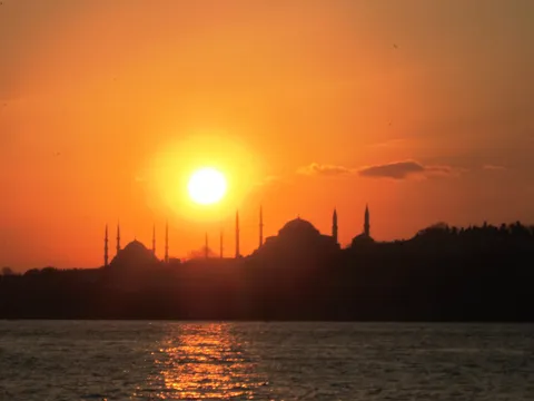 Silhouettes of the Blue Mosque and Hagia Sophia domes and minarets against an orange sunset sky