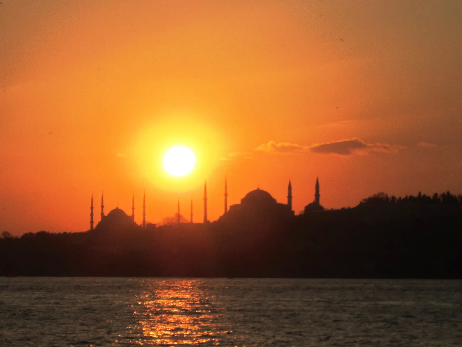 Silhouettes of the Blue Mosque and Hagia Sophia domes and minarets against an orange sunset sky