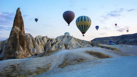 Dozens of hot air balloons rising over Cappadocia's rock formations at sunrise