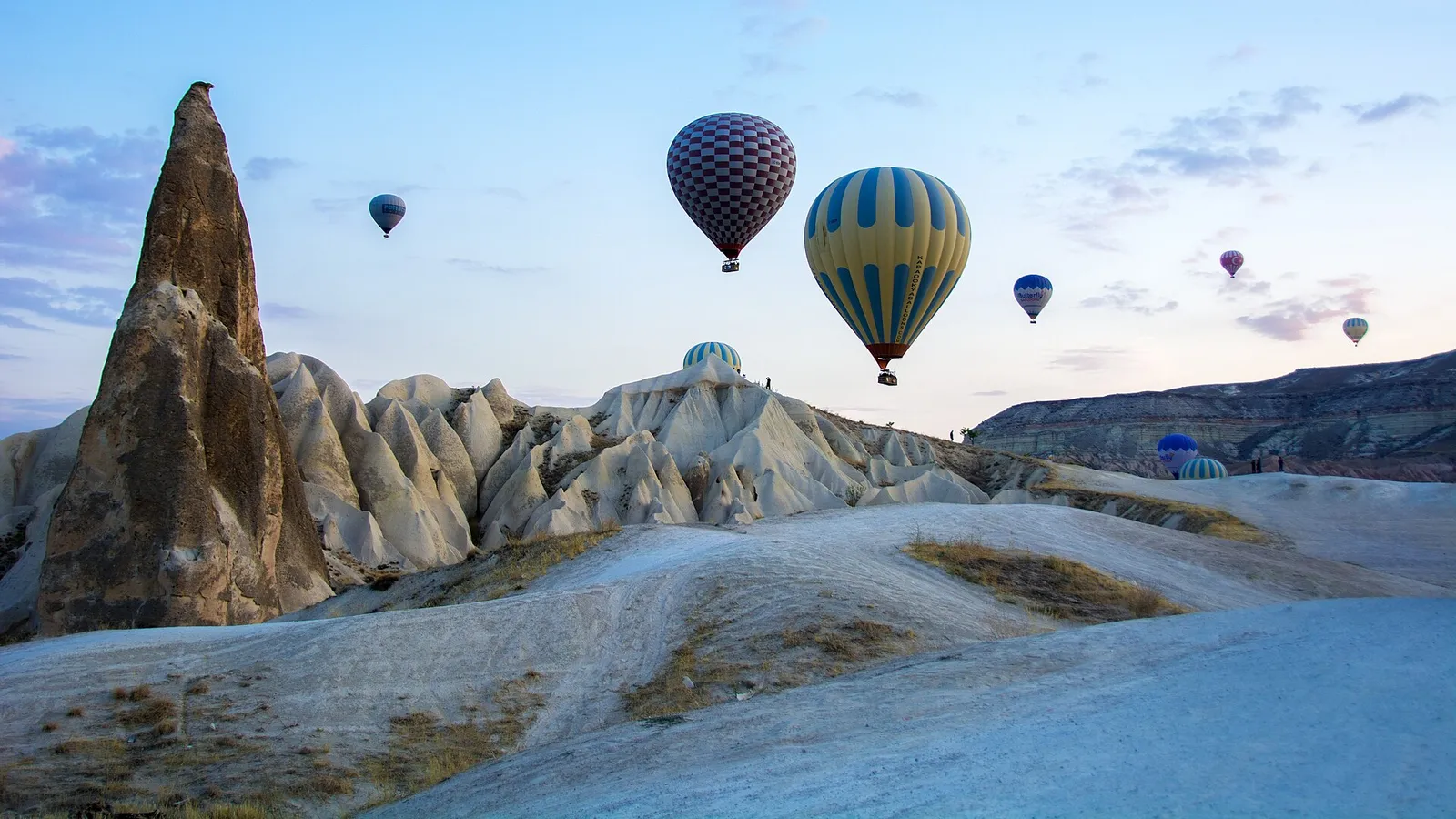 Dozens of hot air balloons rising over Cappadocia's rock formations at sunrise