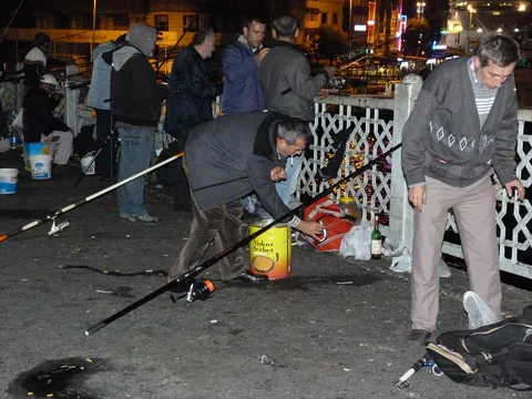 Fishermen silhouetted along Galata Bridge's railing at night with city lights behind them
