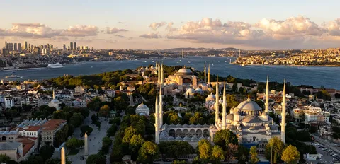 Wide aerial view of Istanbul's historic peninsula with domed mosques beside the Bosphorus and the modern skyline beyond